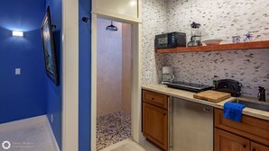 Eine Küche mit Mikrowelle, Toaster, Mixer und Kaffeemaschine auf der Arbeitsplatte. Ein Holzschneidebrett und ein blaues Geschirrtuch hängen an der Ofentür. Die Küche hat eine geflieste Spritzschutzwand und Holzschränke.