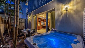 A hot tub in a backyard with a dining area and a view into a house.