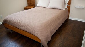A neatly made bed with a wooden headboard, a small chair, and a bedside table with a lamp.