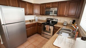 A kitchen with wooden cabinets, a stainless steel refrigerator, a microwave, an oven, a sink, and a dish rack.