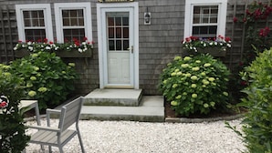 A building with a white door and windows, a nameplate reading "SAMTUCKET", and flower boxes with red and white flowers.