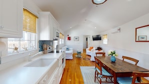 A modern kitchen with white cabinetry, a wooden dining table, and a living area with white furniture.