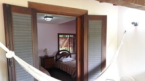 Een kamer met een bed, nachtkastje, lamp, stoel en een hangstoel.