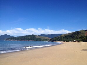 Una playa con cielo despejado, mar tranquilo y colinas verdes al fondo.