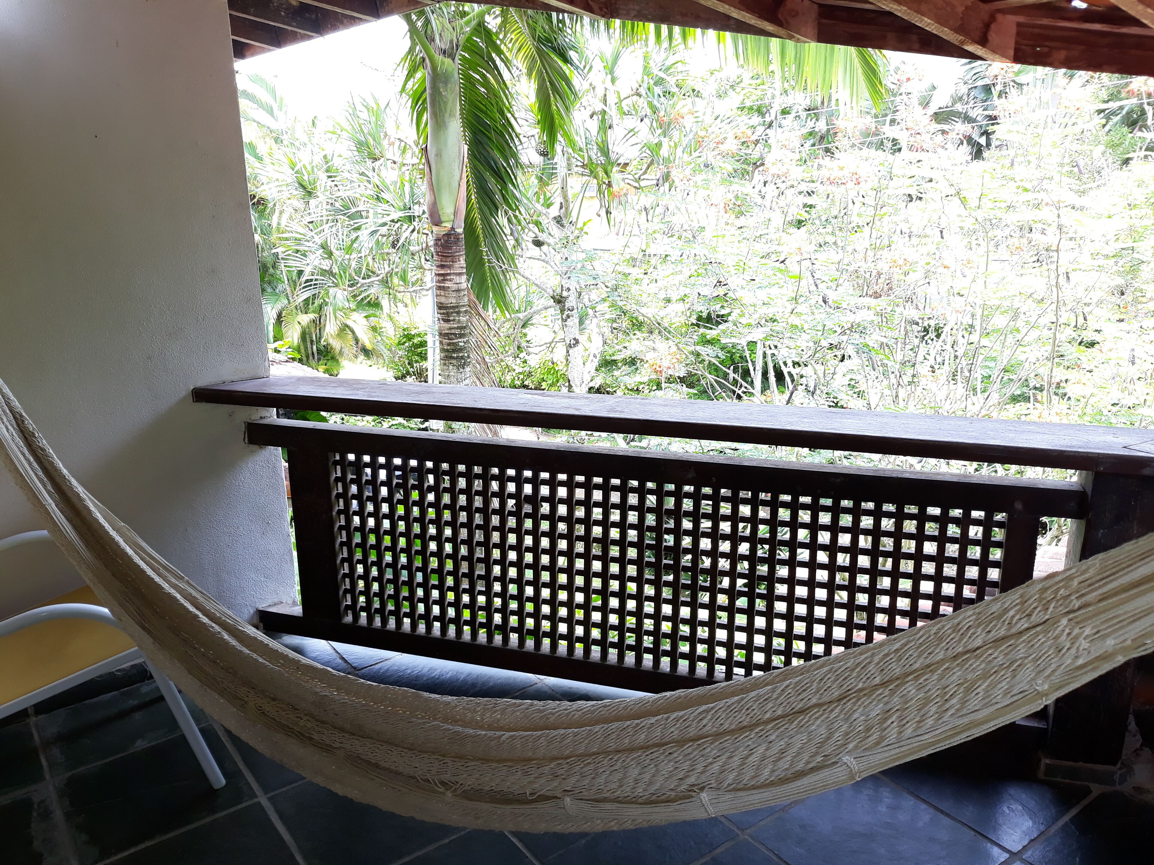 A hammock chair in a covered outdoor area with a view of tropical vegetation.