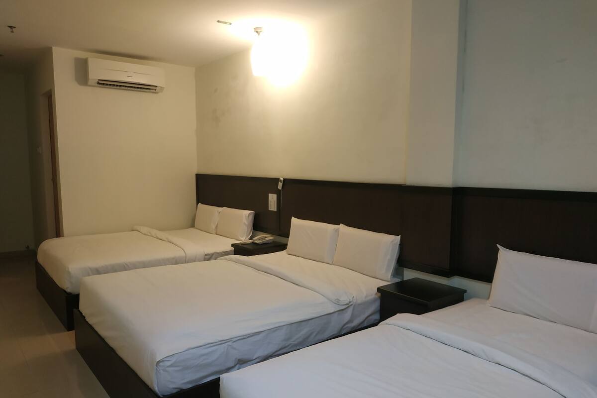Habitación de hotel con dos camas individuales, una mesita de noche con teléfono y un equipo de aire acondicionado en la pared.