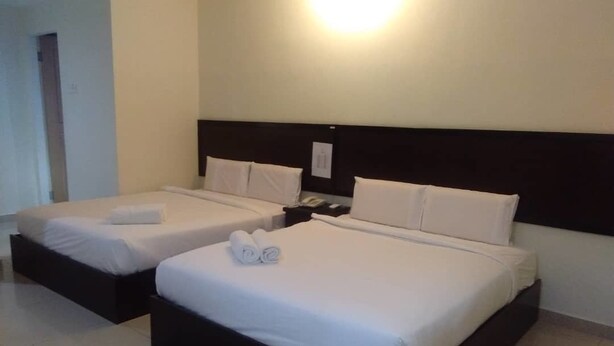 Habitación de hotel con dos camas, cada una con sábanas y almohadas blancas, cabecero oscuro y mesita de noche con teléfono.
