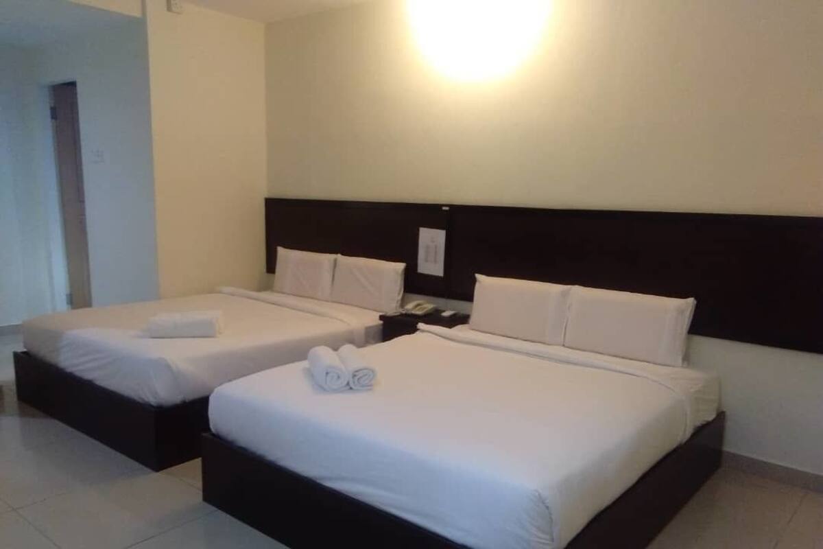 Habitación de hotel con dos camas, cada una con sábanas y almohadas blancas, cabecero oscuro y mesita de noche con teléfono.