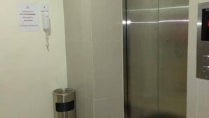 Un ascensor con acabados metálicos, un interfono en la pared y un cubo de basura.