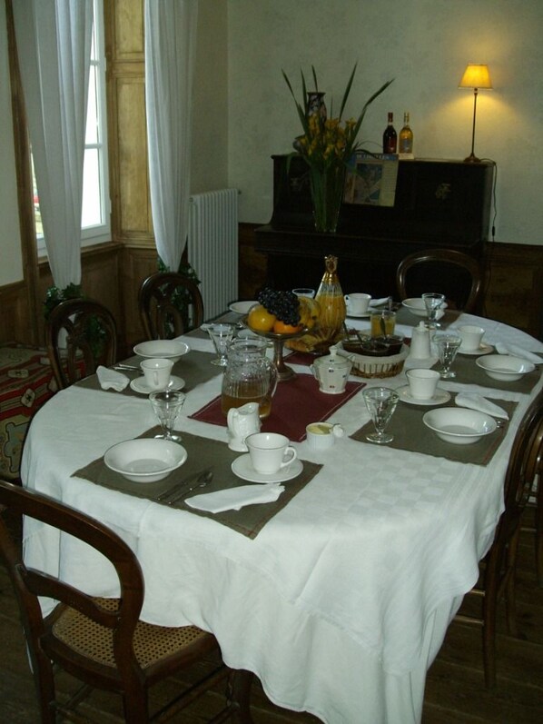 Una mesa de comedor preparada para una comida, con manteles blancos, platos, vasos y una jarra de jugo.