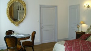A bedroom with a bed, a round table with chairs, a mirror, and two doors. - Chambre d'hôtes - Domaine De Berthegille (Sablonceaux)