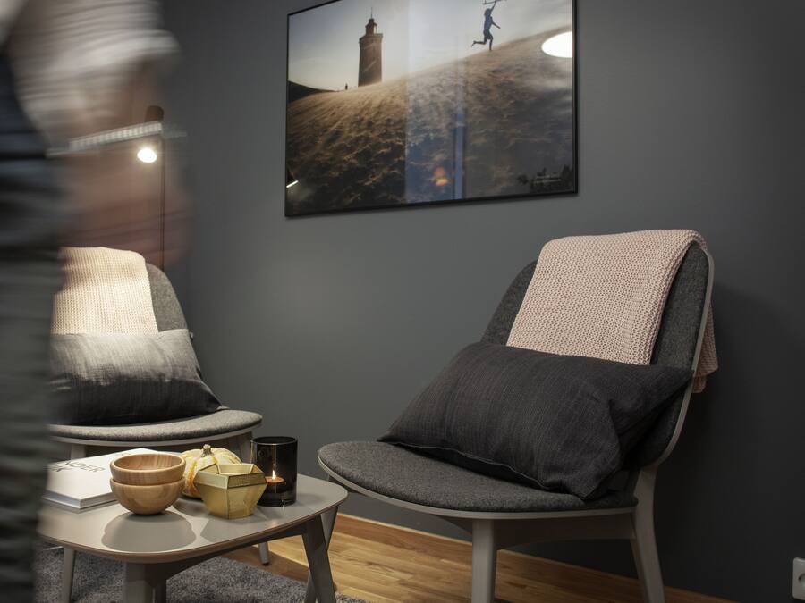 Una sala moderna con dos sillones grises, una mesita con un cuenco, una vela y un libro. En la pared, un cuadro enmarcado de un faro.