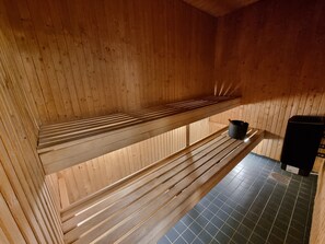 Una sauna de madera con bancos y un recipiente negro.