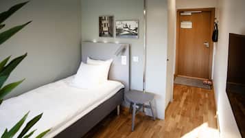 A neatly arranged bedroom with a bed, a small stool, and a door leading to another room.