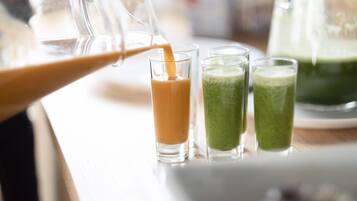 A pitcher pouring a beverage into a glass, with two other glasses containing different colored drinks on a table.