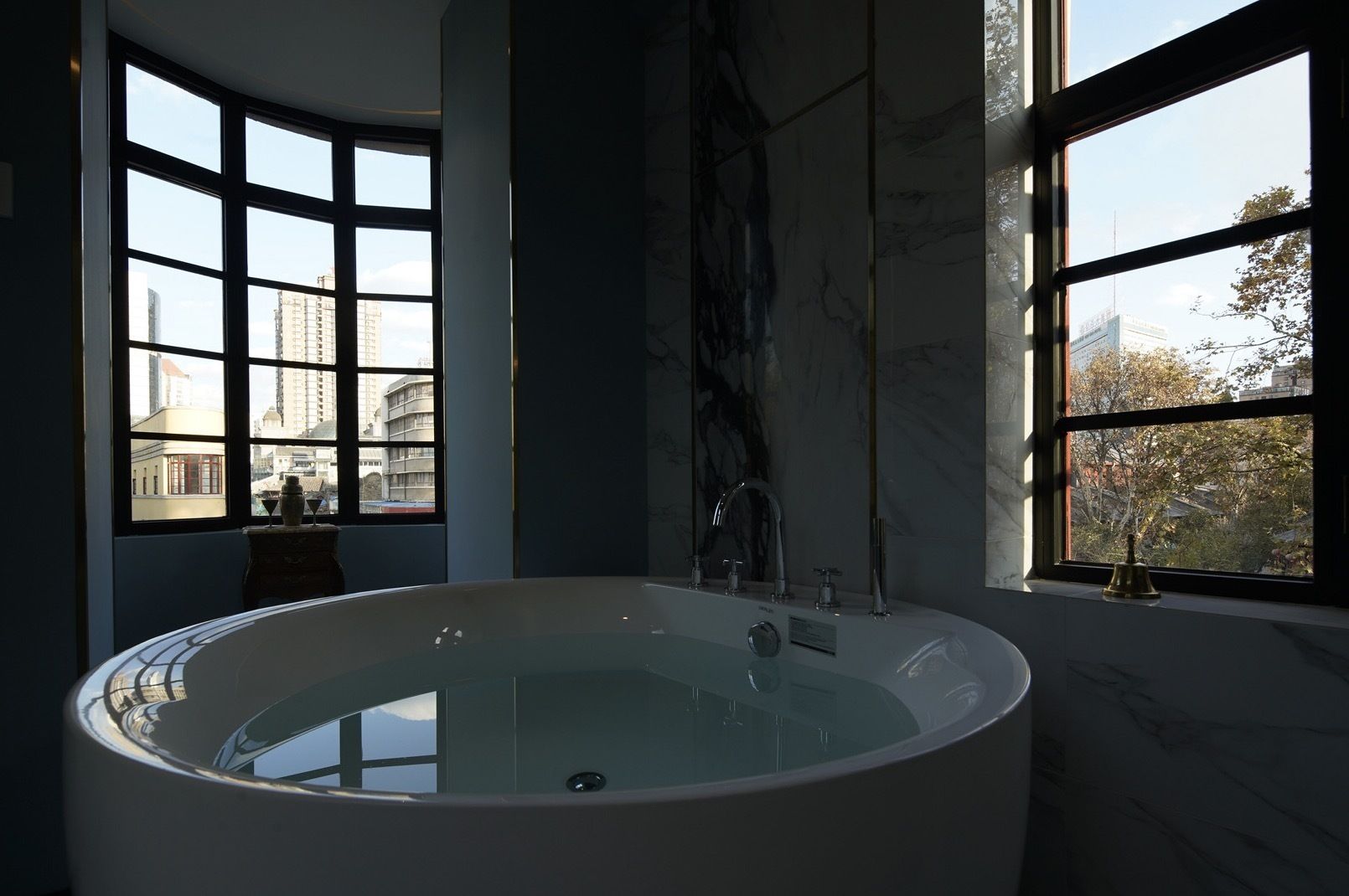A modern bathroom with a freestanding bathtub, large windows, and a view of the cityscape.