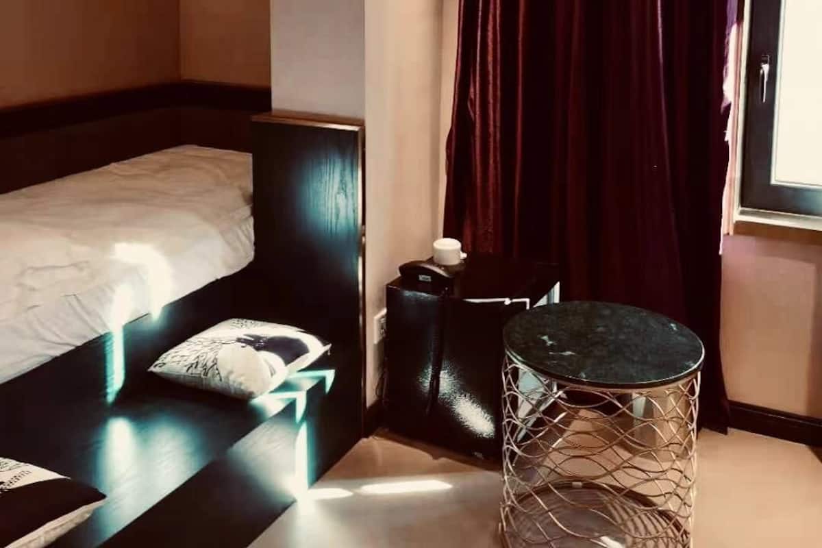 Hotellihuone, jossa on sänky, pieni pöytä, koristeellinen metallijakkara ja ikkuna, jossa on verhot.