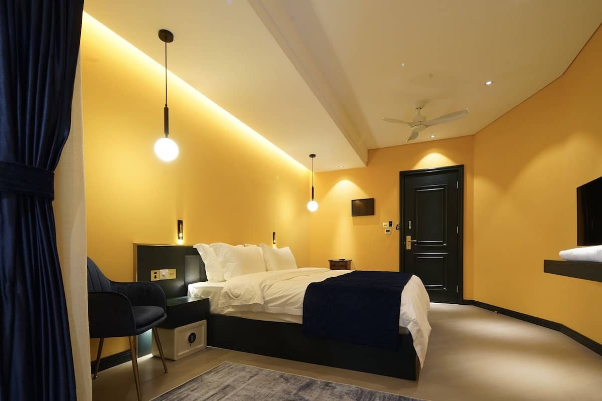 Moderni hotellihuone, jossa on sänky, yöpöydät, työpöytä, tuoli, kattotuuletin ja televisio.