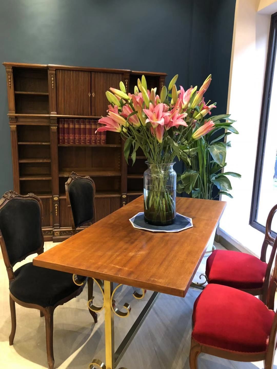 A wooden table with a vase of flowers, surrounded by chairs with black and red cushions.