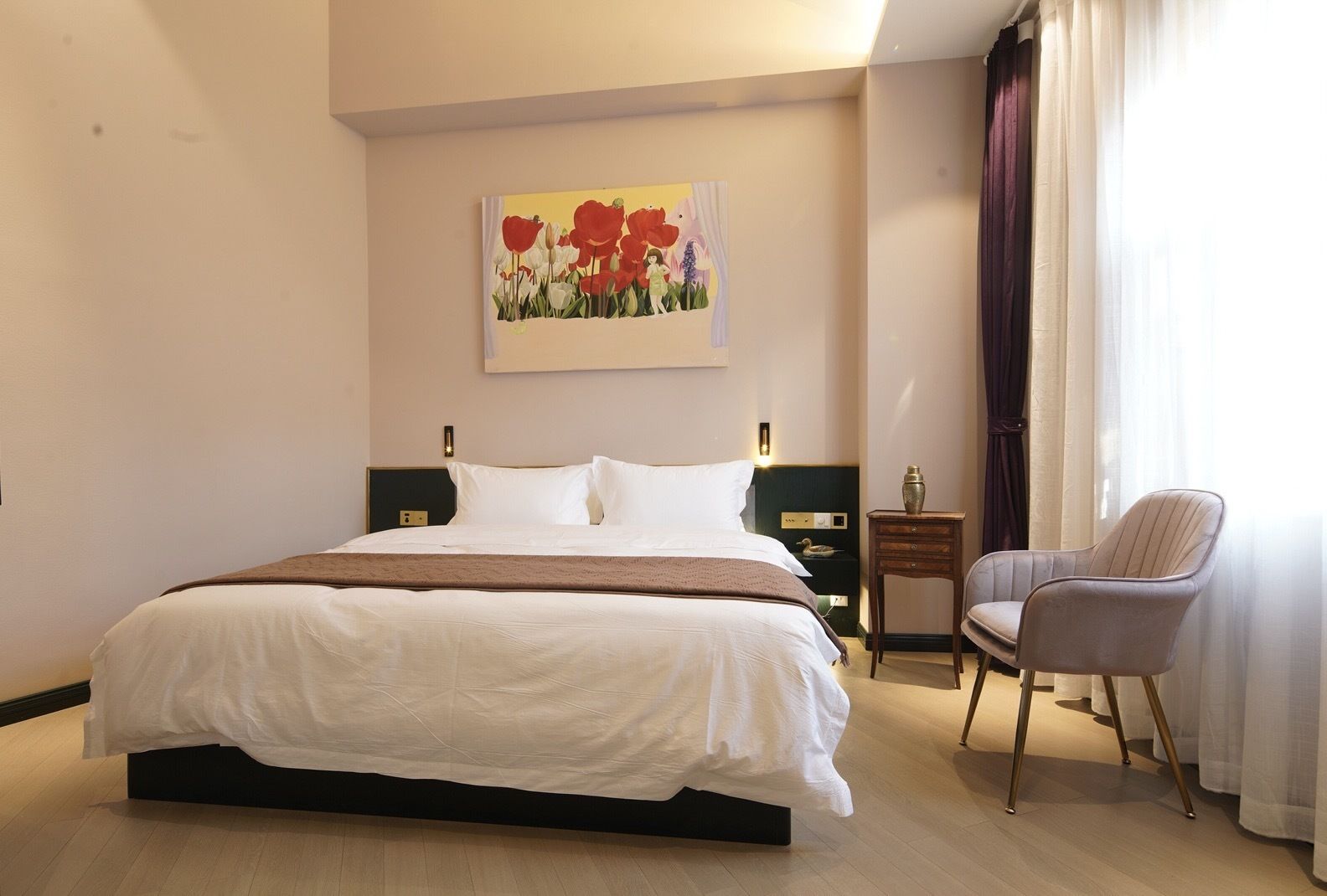 A hotel room with a large bed, a chair, a bedside table, and a painting on the wall.