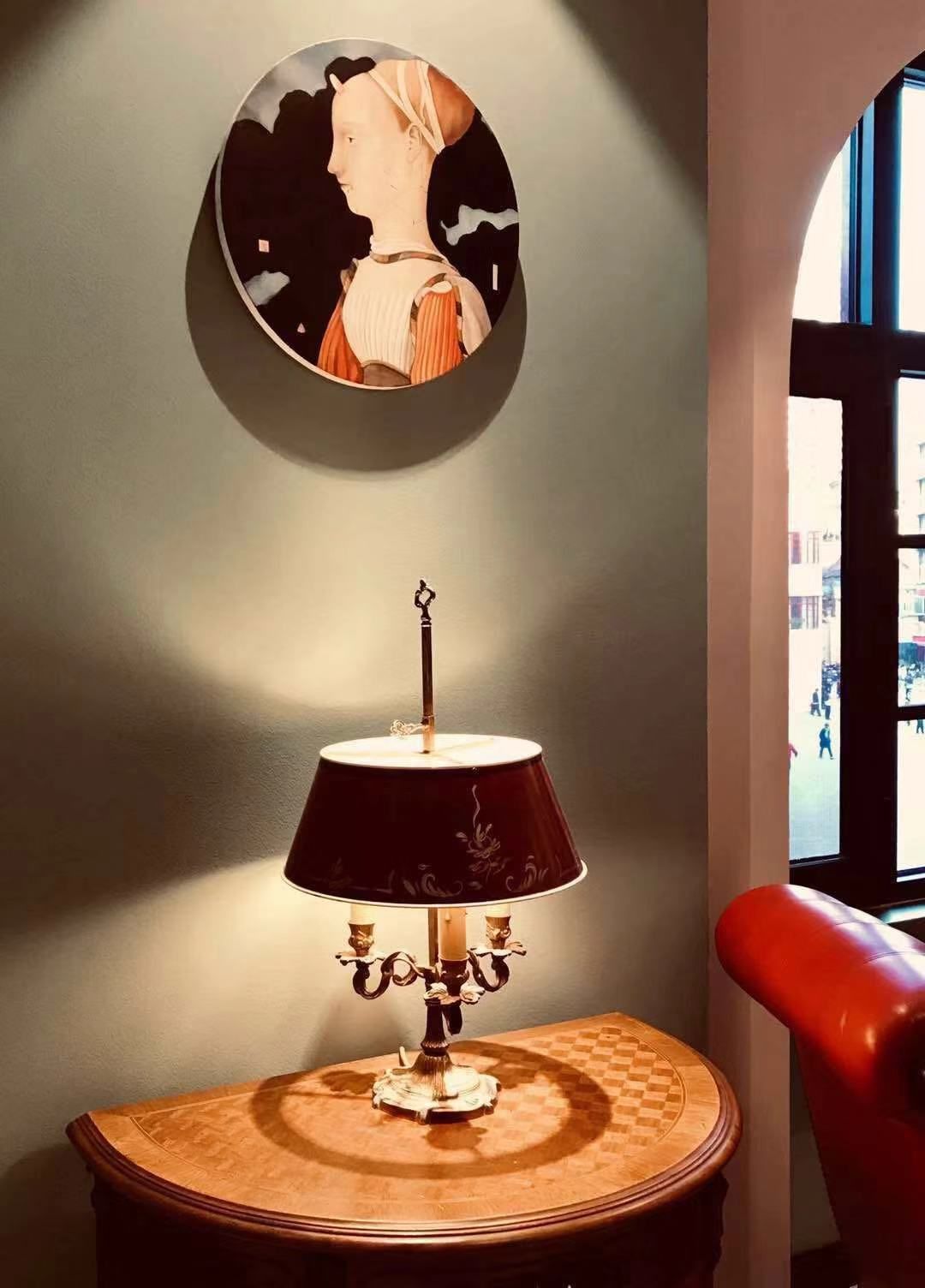 A room with a round table, a lamp, and a wall-mounted painting.