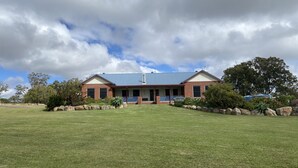 A two-story house with a blue roof, surrounded by a well-maintained lawn and large rocks. - Warwick Country Retreat Pets allowed  (Rosenthal Heights)