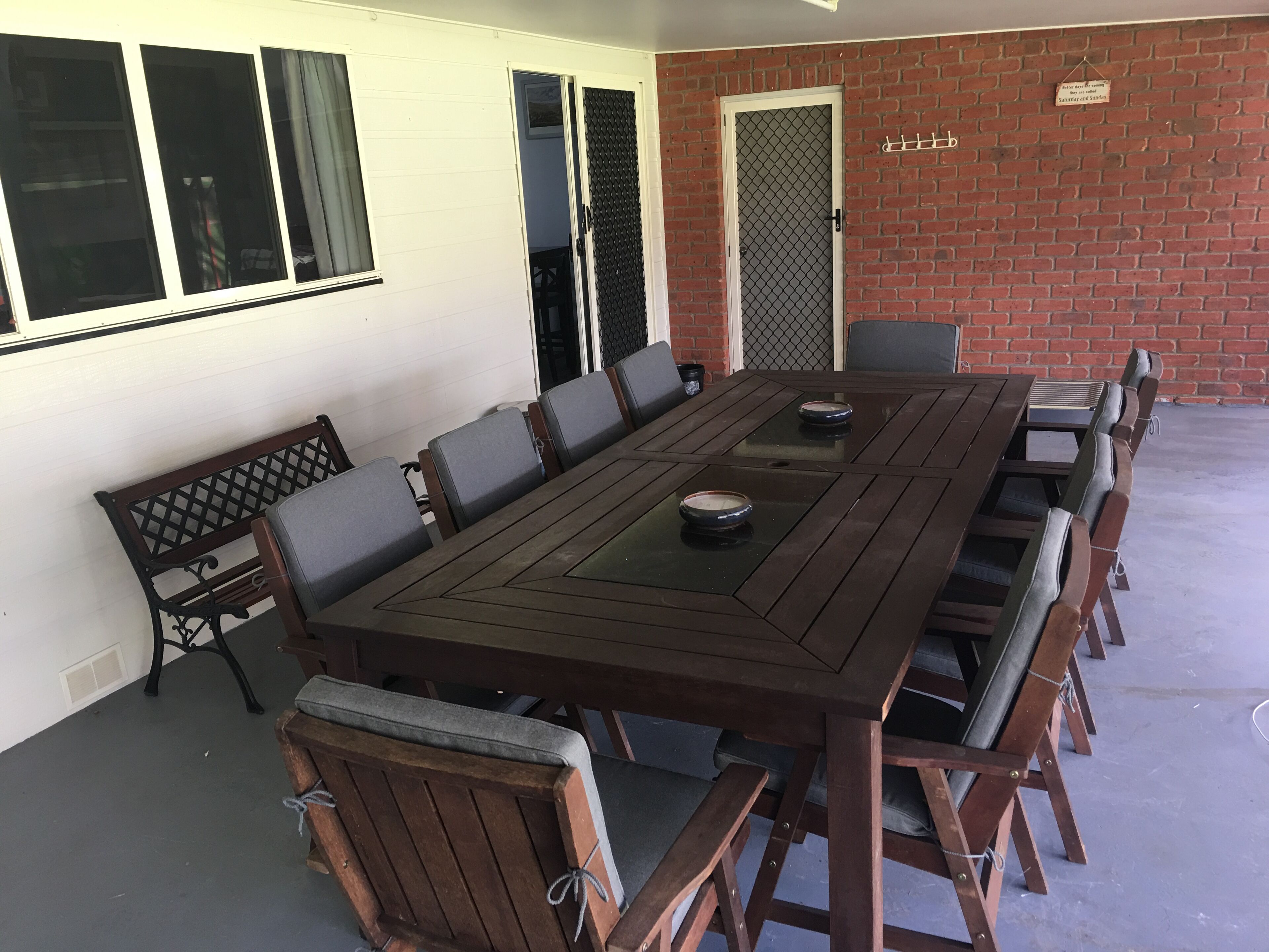 A rectangular outdoor dining area with a long table and multiple chairs.