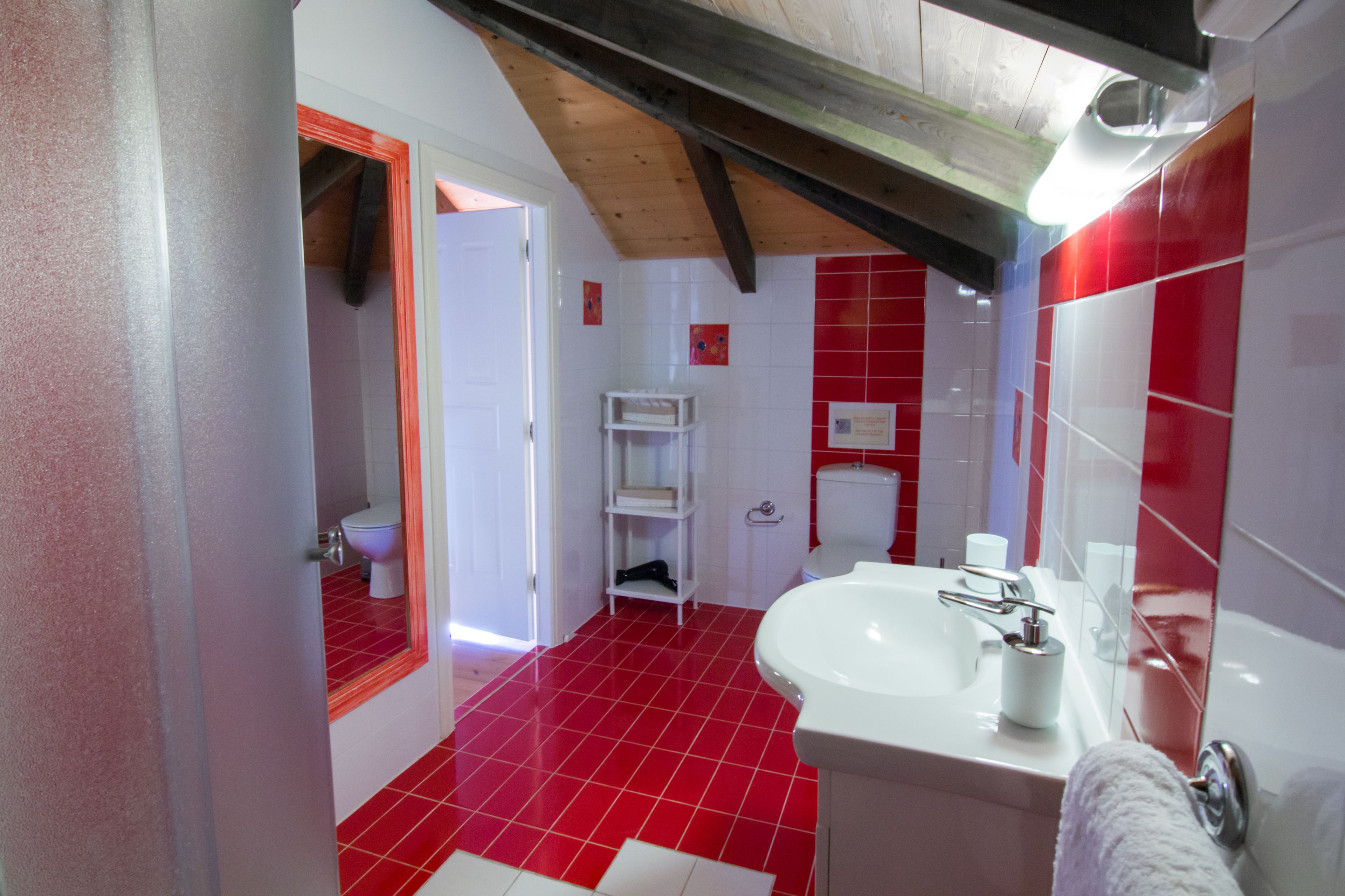 A bathroom with red tiles, a white sink, and a white toilet.