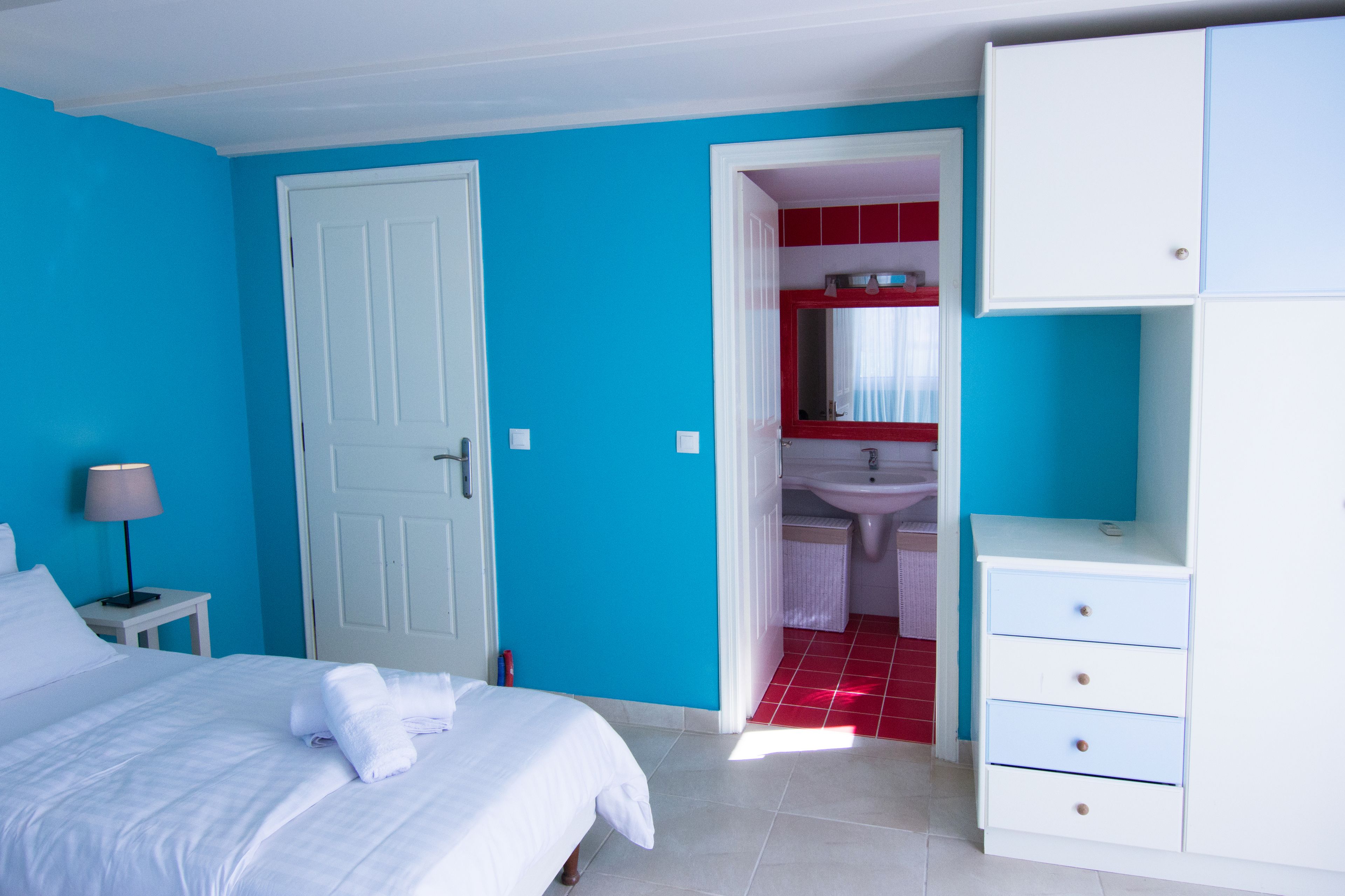 A bedroom with a bed, a nightstand, a wardrobe, and a bathroom visible through an open door.