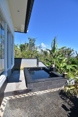 Un área de piscina moderna al aire libre con un deck de piedra y una pequeña fuente de agua.