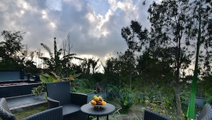 An outdoor seating area with wicker chairs and a table, surrounded by lush greenery and a cloudy sky. - Wanagiri Cosmic Nature Villa (Wanagiri)