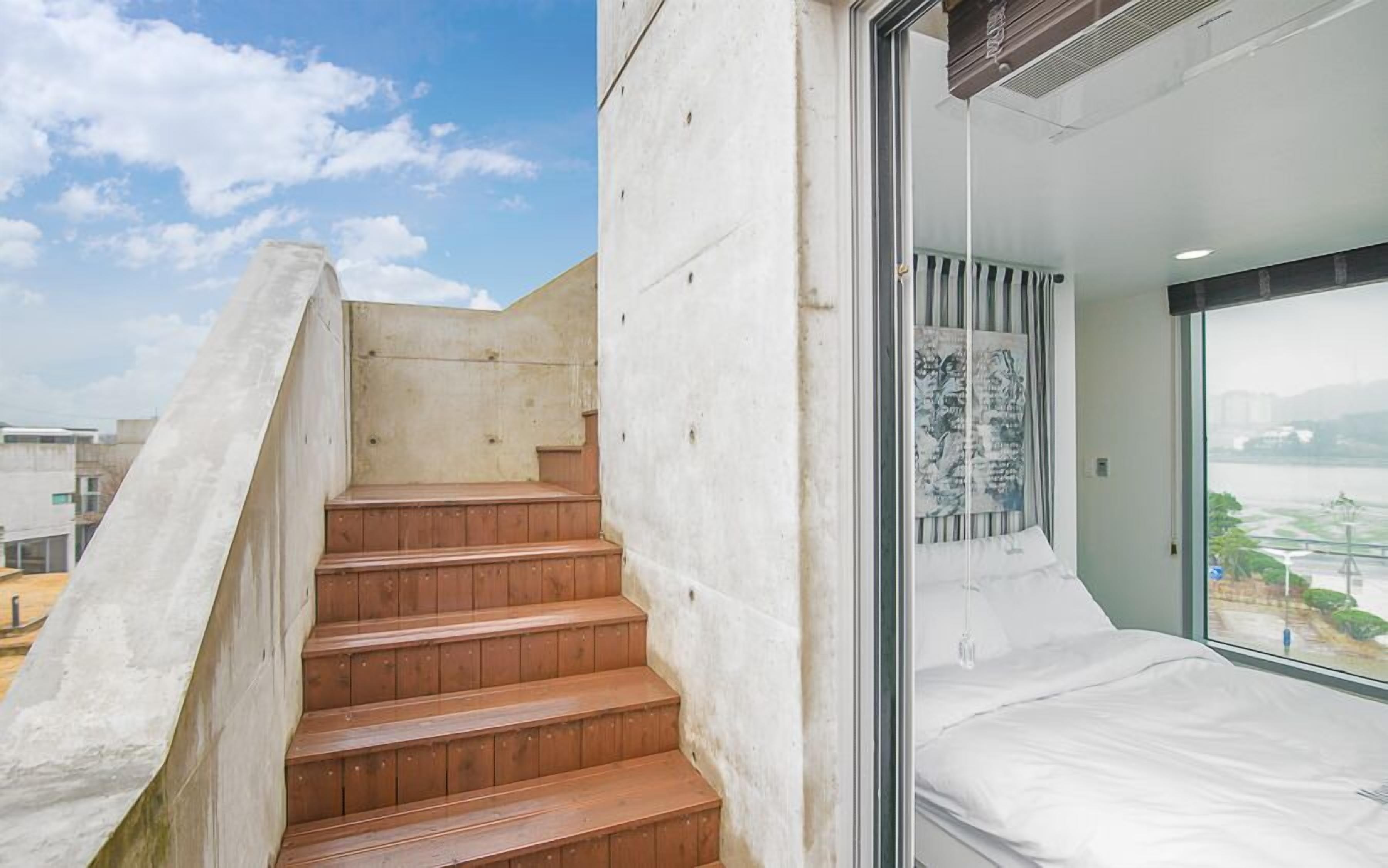 Ein modernes Hotelzimmer mit großem Fenster, einem Bett und einer Treppe, die zu einem Außenbereich führt.