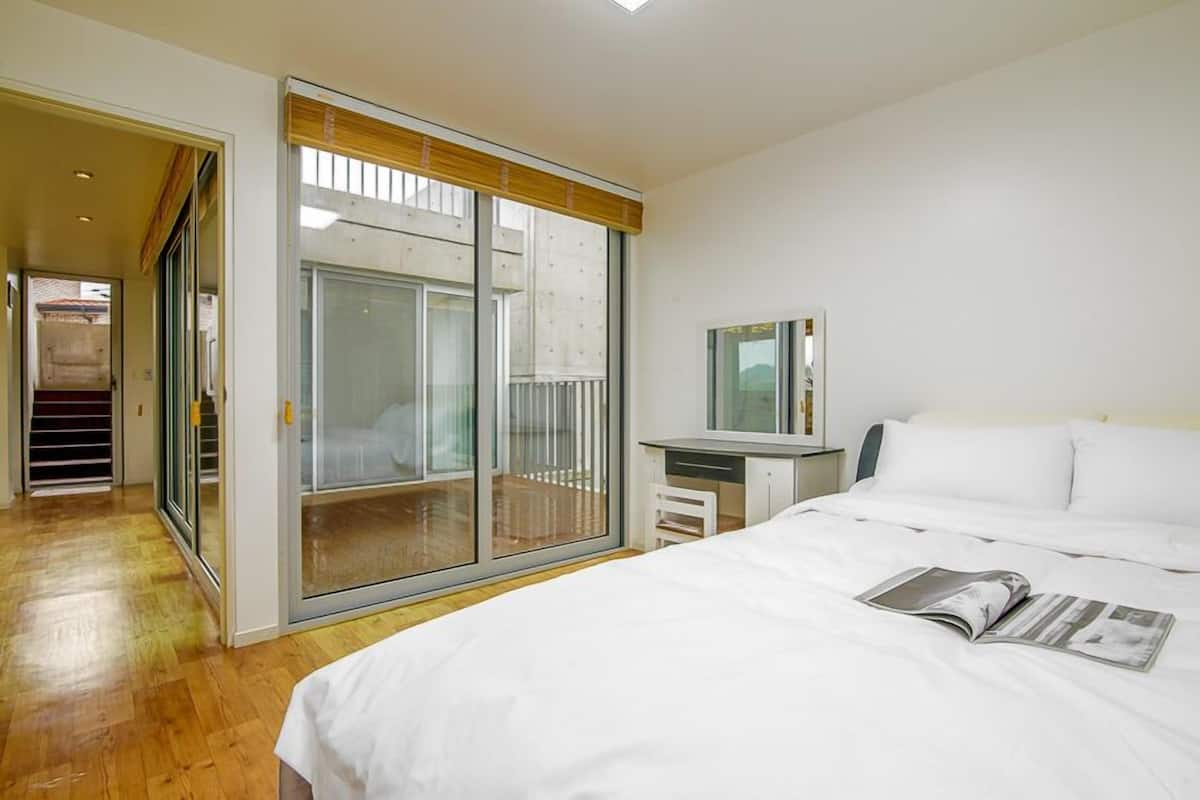 A modern hotel room with a large bed, a desk, and a sliding glass door leading to a balcony.