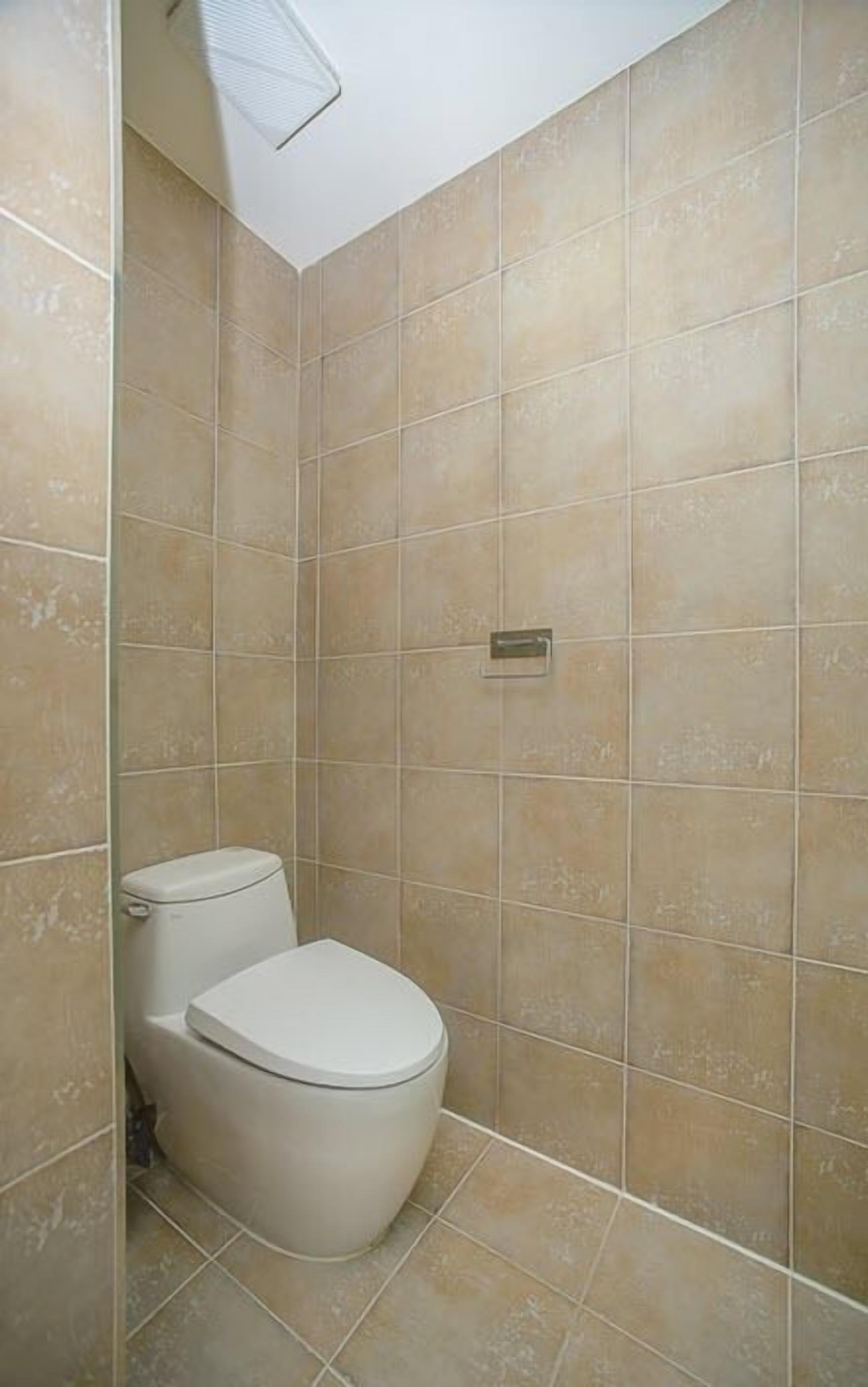 Baño con azulejos color beige, inodoro y zona de ducha.