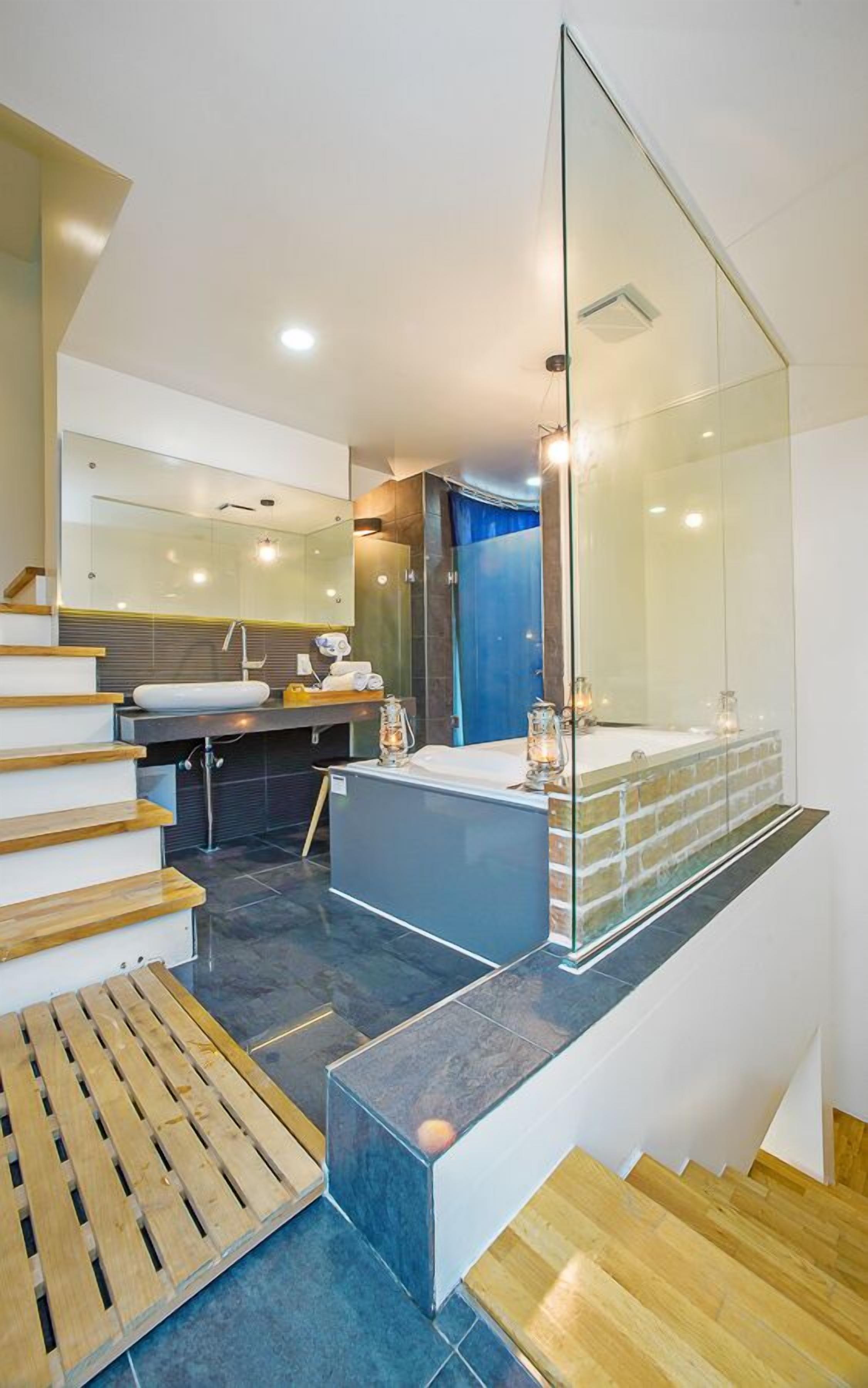 Un baño moderno con cabina de ducha de vidrio, un espejo grande y una escalera de madera.