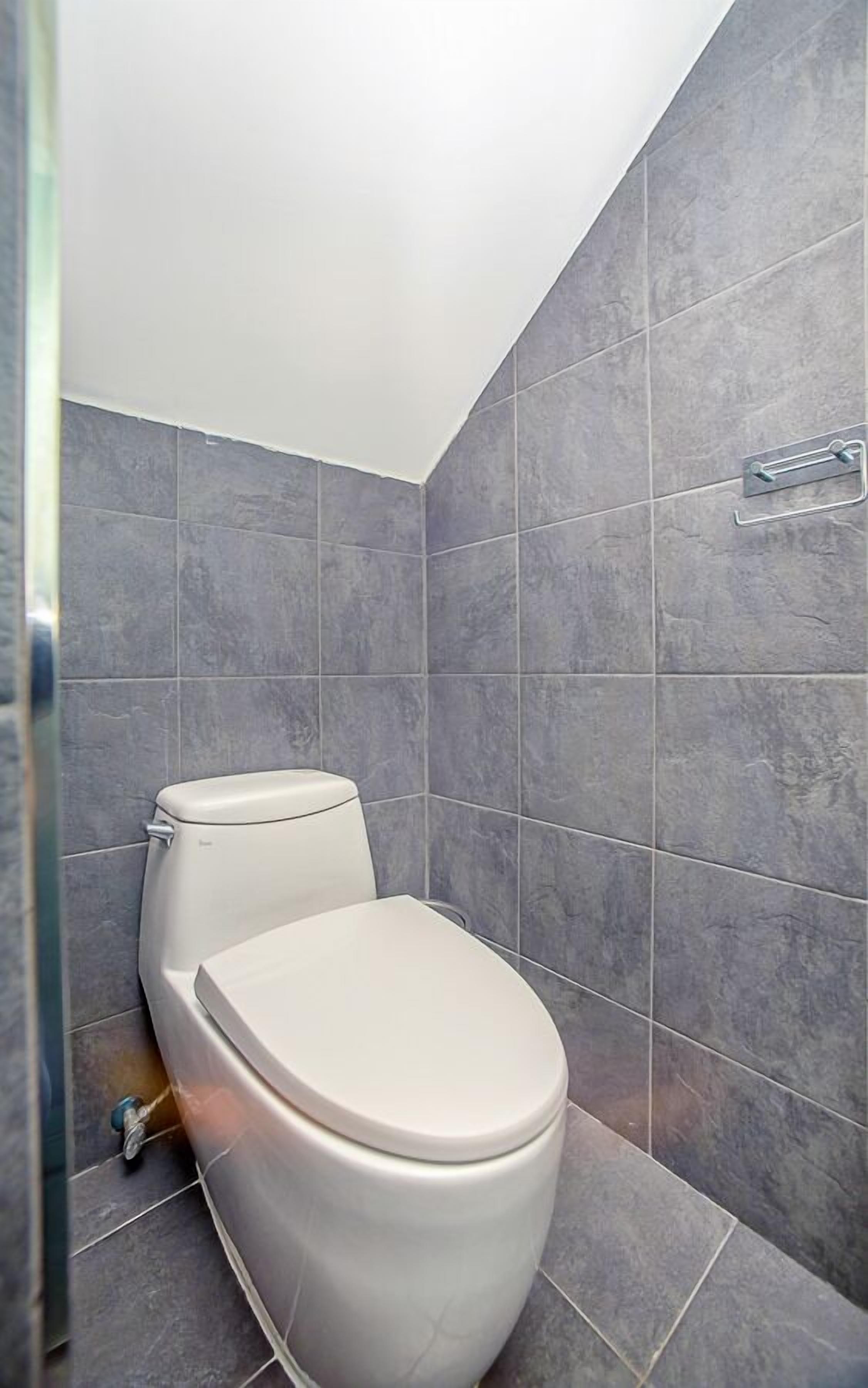 A modern bathroom with a white toilet, grey tiles, and a shower area.
