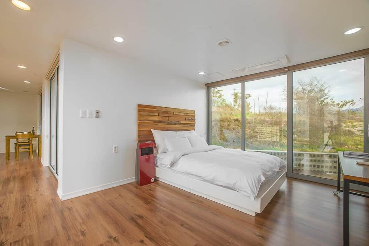 A modern bedroom with a wooden headboard, a large window, and a view of the outdoors.