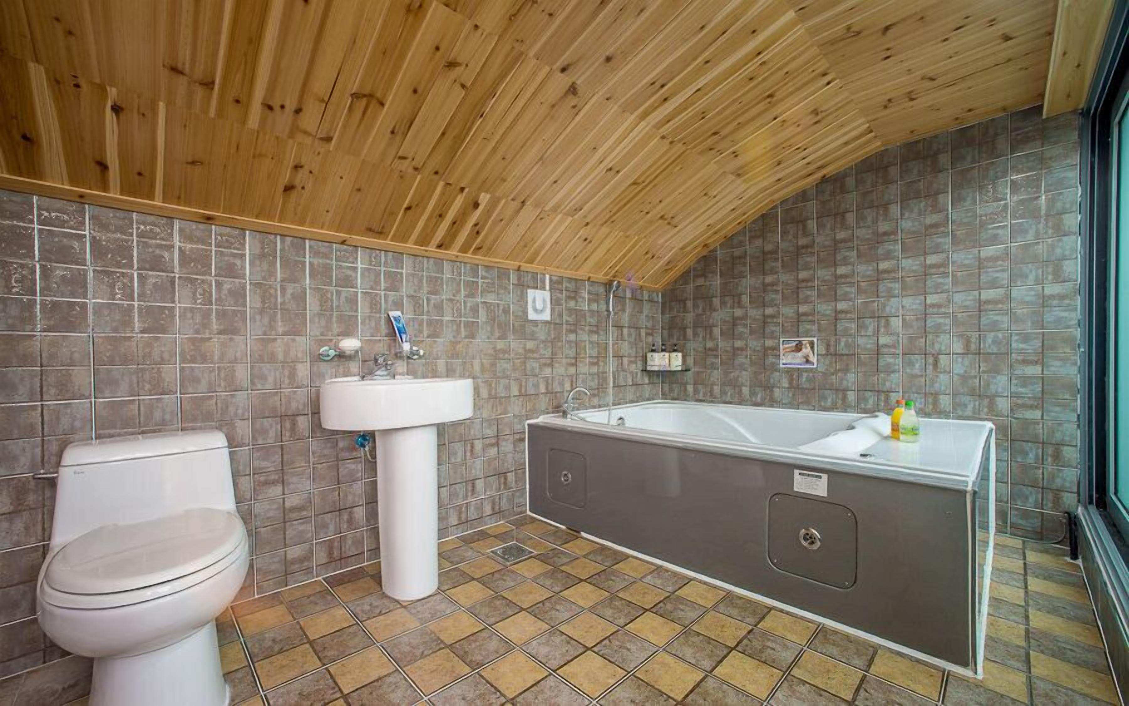 Un baño con techo de madera, inodoro, lavabo y bañera.