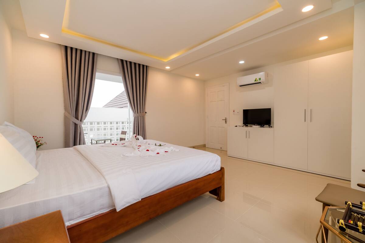 A modern bedroom with a wooden bed, a flat-screen TV mounted on the wall, and a view of buildings outside.