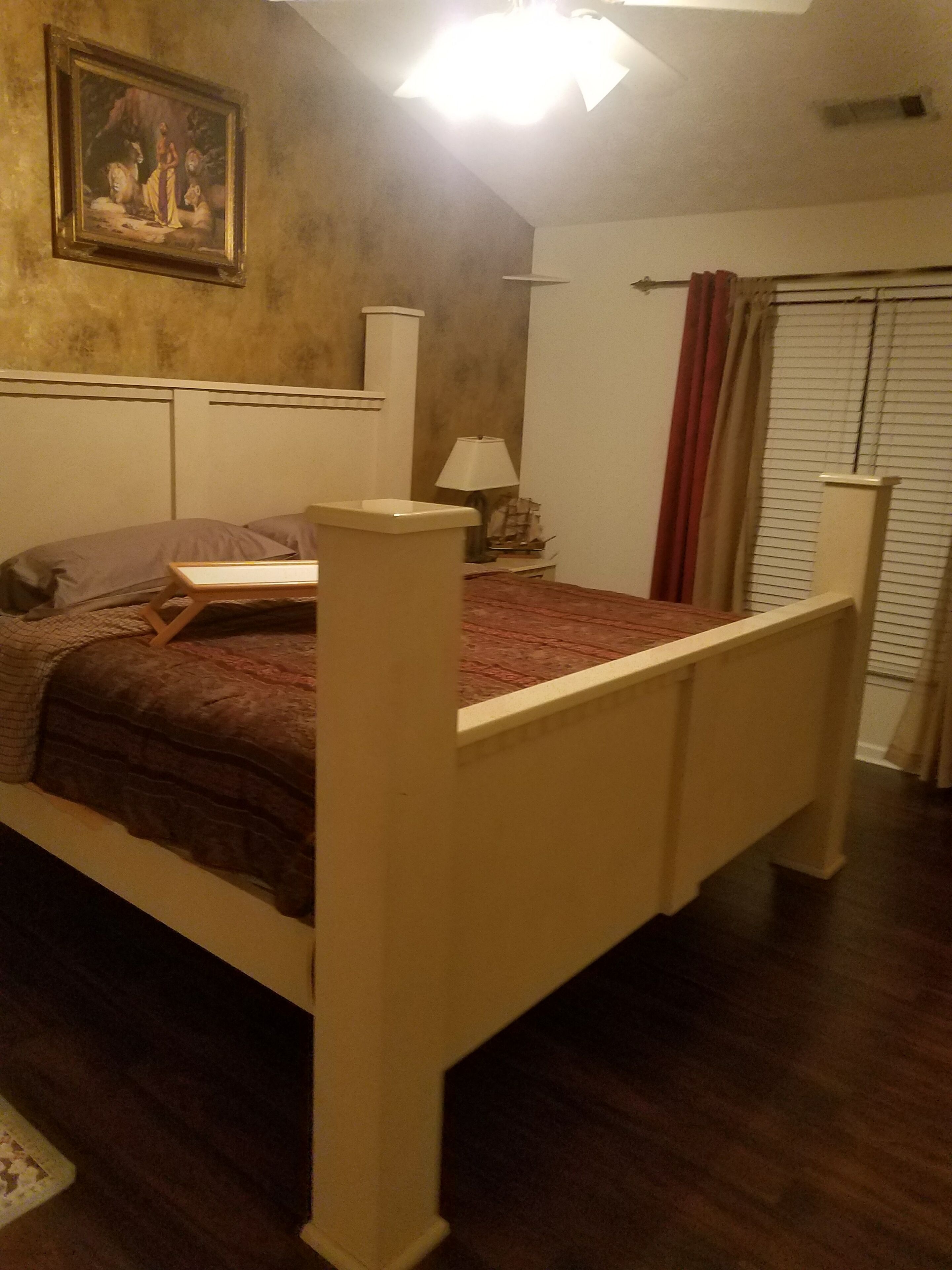 Een slaapkamer met een houten bed, een nachtkastje, een lamp en een schilderij aan de muur.