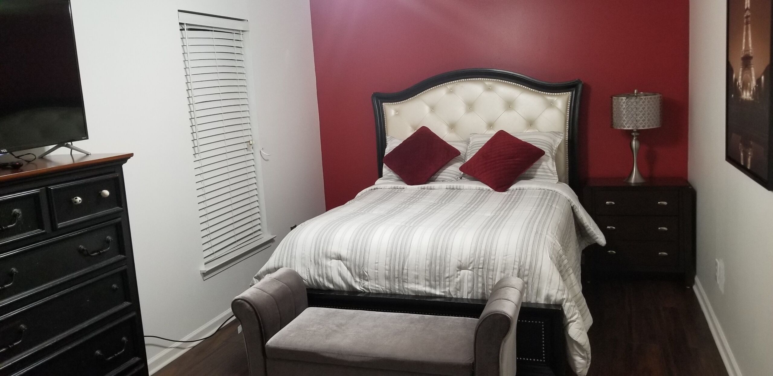 A bedroom with a bed, a nightstand, a lamp, a TV, and a dresser.