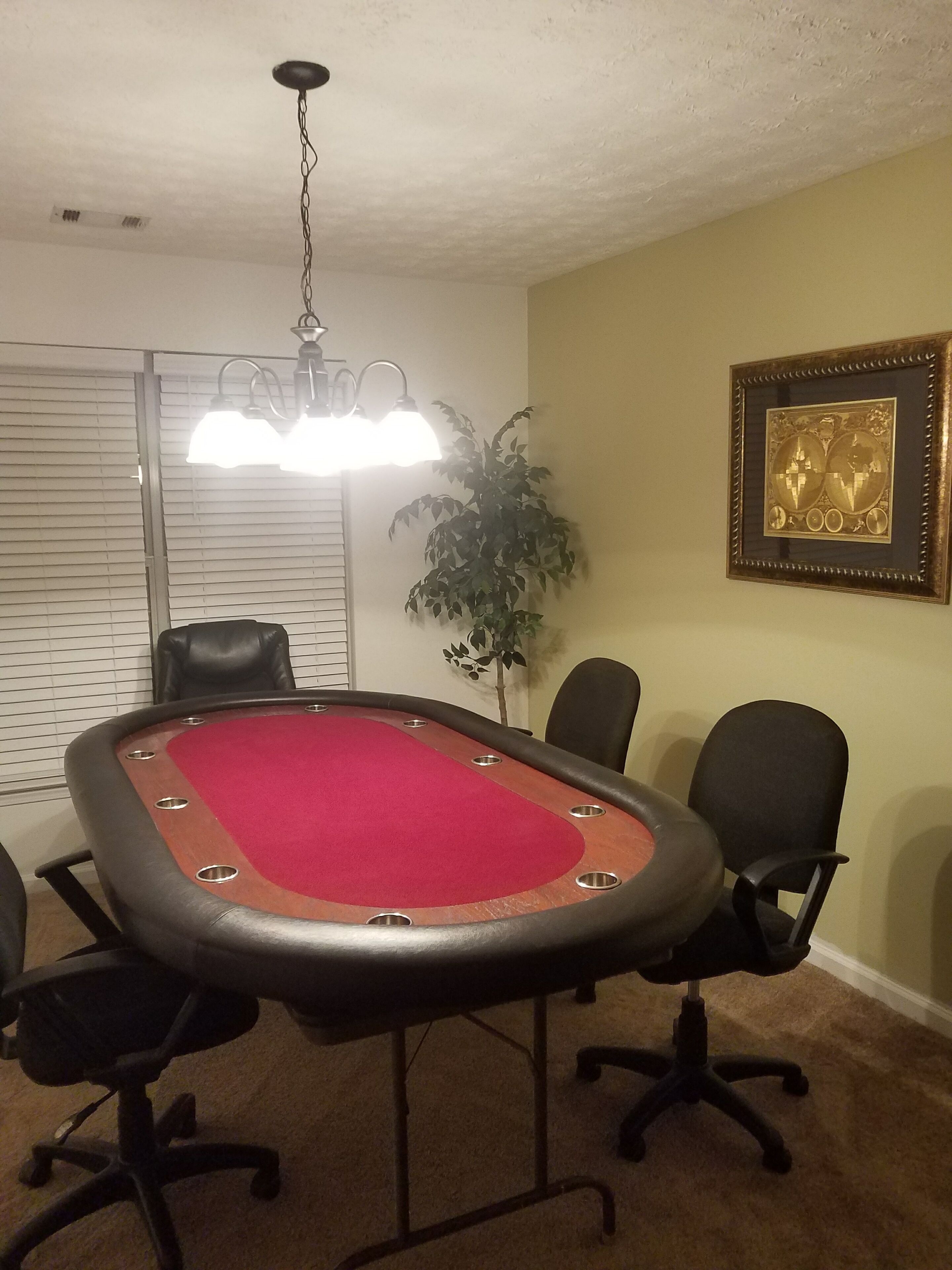 A conference room with a pool table, black chairs, a potted plant, and a framed artwork on the wall.