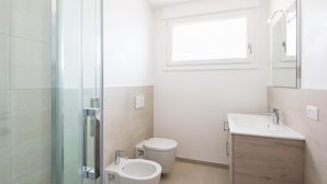 Een moderne badkamer met een glazen douchecabine, toilet, bidet en een wastafel met spiegel.