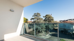 Een modern appartement met een ruim balkon, een betegelde vloer en vrij uitzicht op straat en bomen.