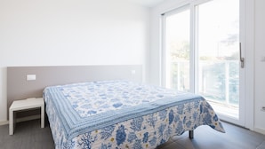 Een slaapkamer met een bed, een klein nachtkastje en een grote schuifdeur naar een balkon.