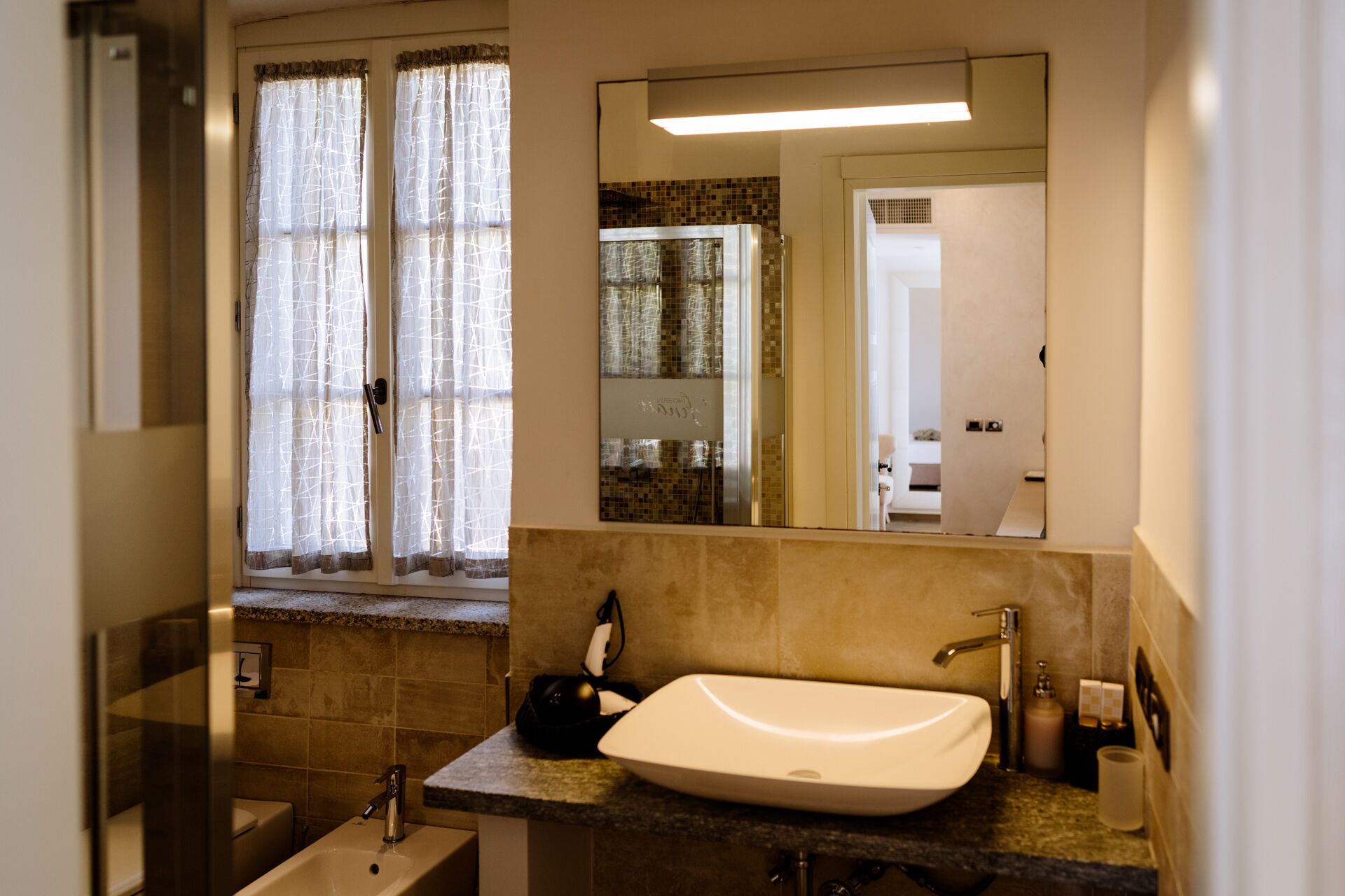 A bathroom with a white sink, a mirror above it, and a window with curtains.