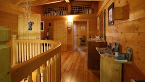 Interior d'una cabana de fusta amb escala de fusta, zona alta amb prestatgeries i menjador amb taula i cadires.