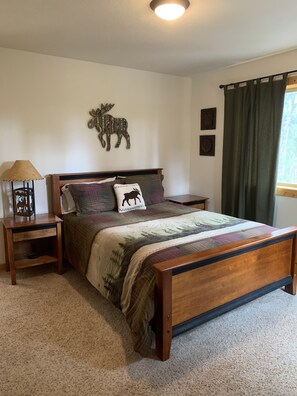 A bedroom with a wooden bed, a nightstand, a lamp, a moose wall decoration, and a window with curtains.