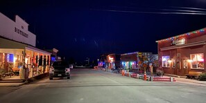 A street lined with buildings, including a distillery and a restaurant with colorful lights.
