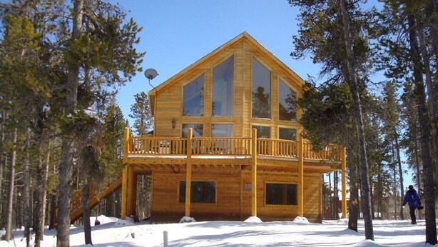 Une cabane en bois dotée d’un balcon, entourée d’arbres et recouverte de neige.